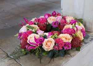 Een liefdevolle rouw krans met mooie materialen met o.a. Gloriosa, Peach Avalanche rozen, Eustoma en Cellosia