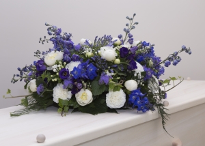Een kistbloemstuk in heldere blauw witte tinten met onder andere Delphinium, witte anjers, Violieren en grootbloemige rozen
